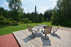 Eine Holzterrasse mit Tisch und vier Stühlen, umgeben von üppiger Vegetation und Bäumen.