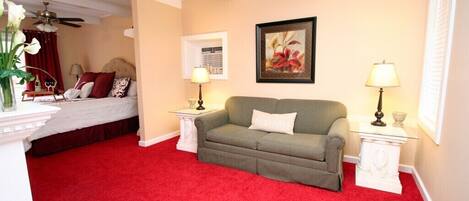 A hotel room with a red carpet, a bed with red curtains, a green sofa, two bedside tables with lamps, and a framed picture on the wall.