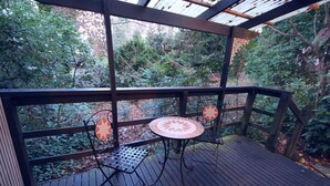 Une terrasse en bois avec une table et deux chaises, entourée d’une balustrade en bois et surmontée d’une verrière.