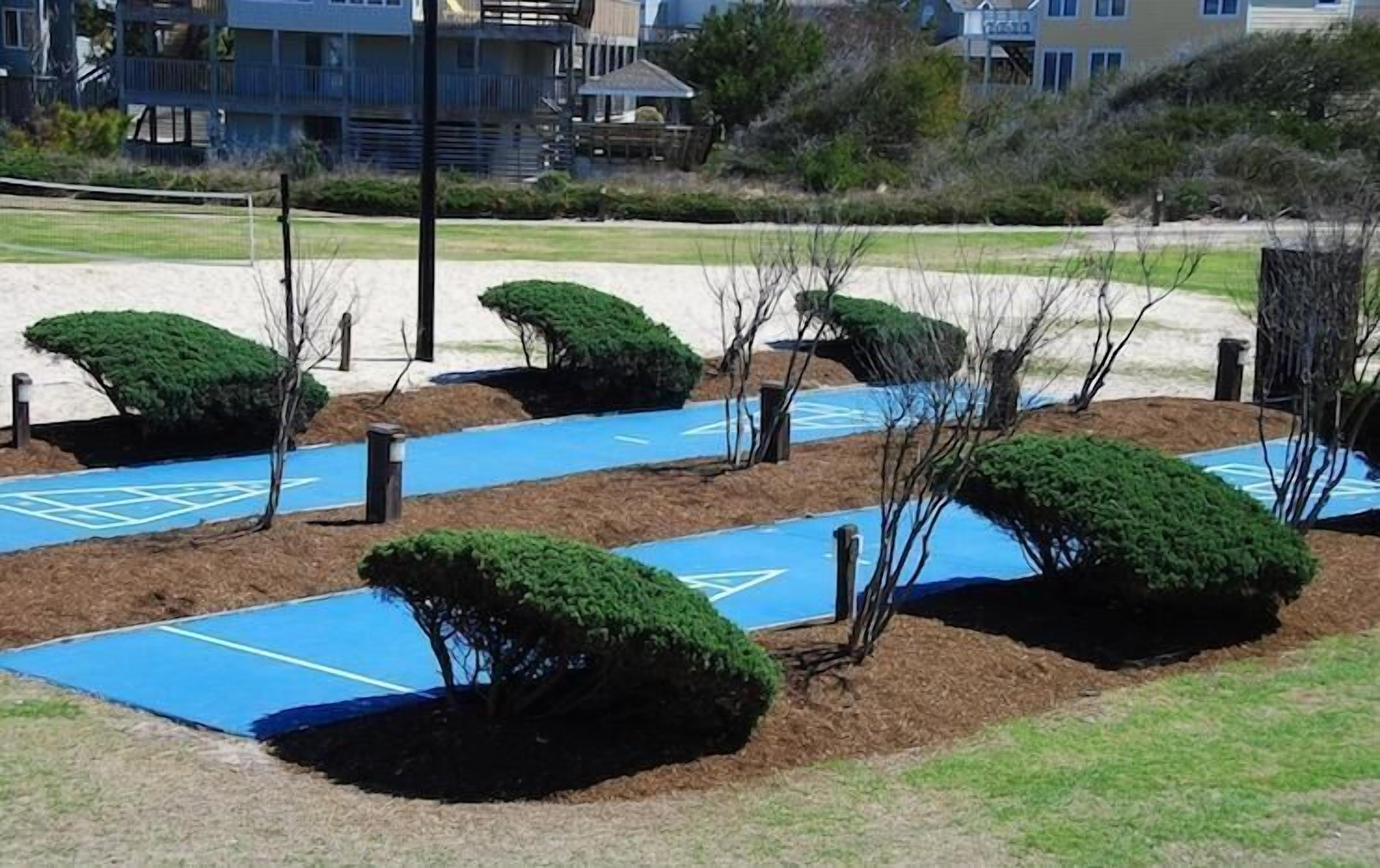 A landscaped area with trimmed bushes and blue mats on the ground, likely for sports or activities.