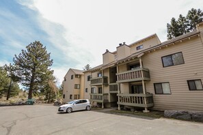 A multi-story apartment building with balconies, a parking lot, and a tree.