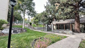Un quartier résidentiel avec un sentier en pierre, un petit jardin fleuri, un banc en bois et un bâtiment doté d’une porte en verre.