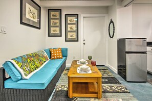 Una sala de estar con un sofá azul, una mesa de centro de madera con posavasos y un refrigerador.