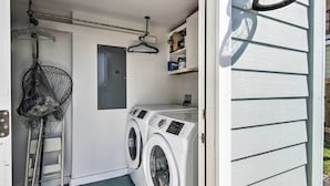 A laundry room with two front-loading washing machines, a drying rack, a hanging clothes rack, and a small shelf with items.