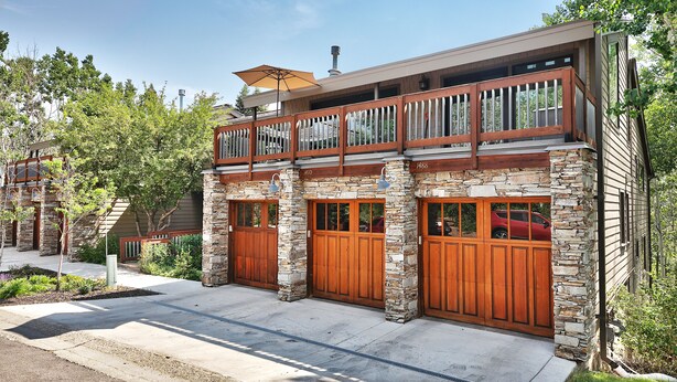 A modern two-story house with a stone facade, wooden garage doors, and a balcony with a wooden railing.