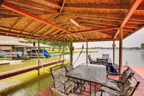 A covered dock with a table and chairs, a boat, and a view of the water.