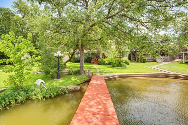 A serene garden with a pond, a wooden bridge, and a building in the background.