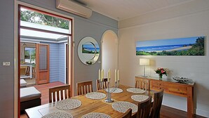 Un coin repas avec une table en bois, des chaises, un miroir, des bougies, un tableau représentant une plage et une vue sur l’extérieur.