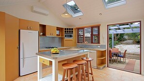 A modern kitchen with a central island, bar stools, a refrigerator, and a microwave. - Harkaway - charming cottage in central Byron Bay (Byron Bay)