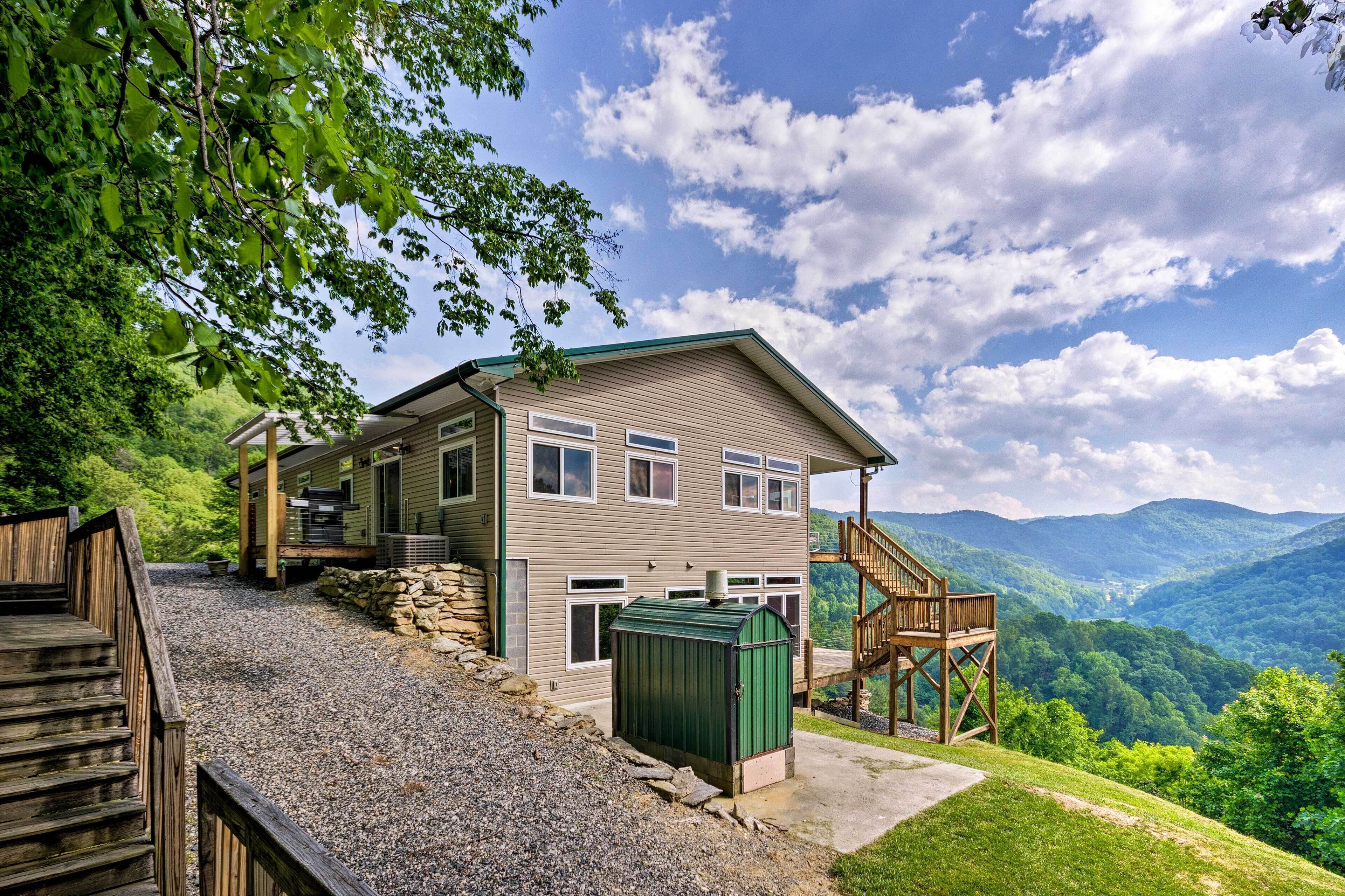 A two-story cabin with a stone foundation, a green metal roof, and a wooden deck.