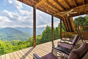 Terraza de madera con dos sillas reclinables y un ventilador de techo, con vistas a un paisaje montañoso.