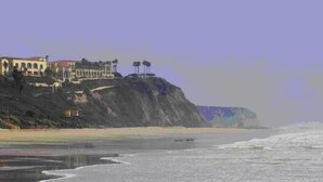 Une vue côtière avec un bâtiment perché sur une falaise, dominant la plage.