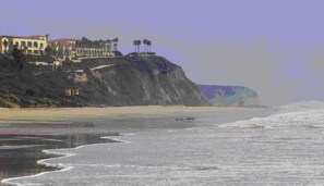Vista costeira com um edifício sobre um penhasco, com vista para a praia.