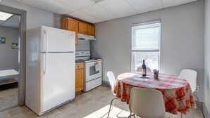 Une cuisine compacte équipée d’un réfrigérateur, d’une cuisinière et de meubles de rangement en bois. On y trouve une table à manger recouverte d’une nappe à carreaux, ainsi que des chaises.