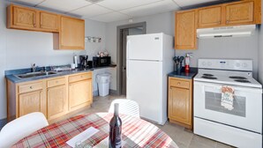 Une cuisine de taille réduite, avec des meubles en bois, un réfrigérateur blanc, une cuisinière et une table à manger recouverte d’une nappe à carreaux.
