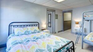 Une chambre d’hôtel comprenant un lit, une table de chevet avec une lampe, un lit superposé et une porte donnant sur une autre pièce.
