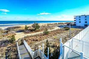 A coastal view with a beach, wooden pathways, and a building with multiple windows.