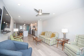 A modern living room with a sofa, chairs, and a coffee table. There is a kitchen in the background with a dining area.