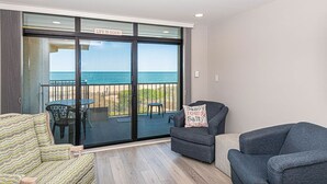 Une pièce avec vue sur l’océan, une porte-fenêtre coulissante, un canapé, un fauteuil et une table avec des chaises à l’extérieur.