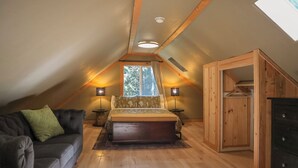 Ein gemütliches Schlafzimmer im Dachgeschoss mit Holzbalkendecke, einem Bett mit floralem Überwurf, einem grünen Sofa und einem Holzschrank.