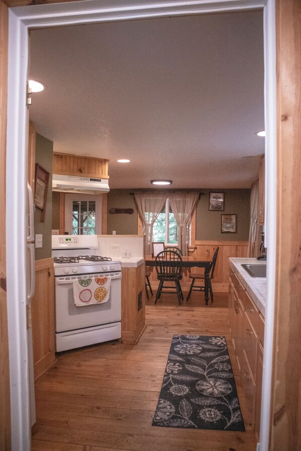 Una cocina compacta con armarios de madera, una estufa, una mesa de comedor con sillas y una ventana con cortinas.