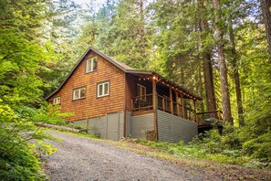 Une cabane dotée d’un porche et d’une terrasse, entourée d’une forêt dense.