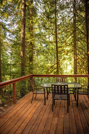 A wooden deck with a table and chairs, surrounded by tall trees.
