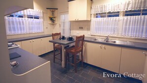 Cocina compacta con zona de comedor, que incluye estufa, lavamanos y dos sillas de madera.