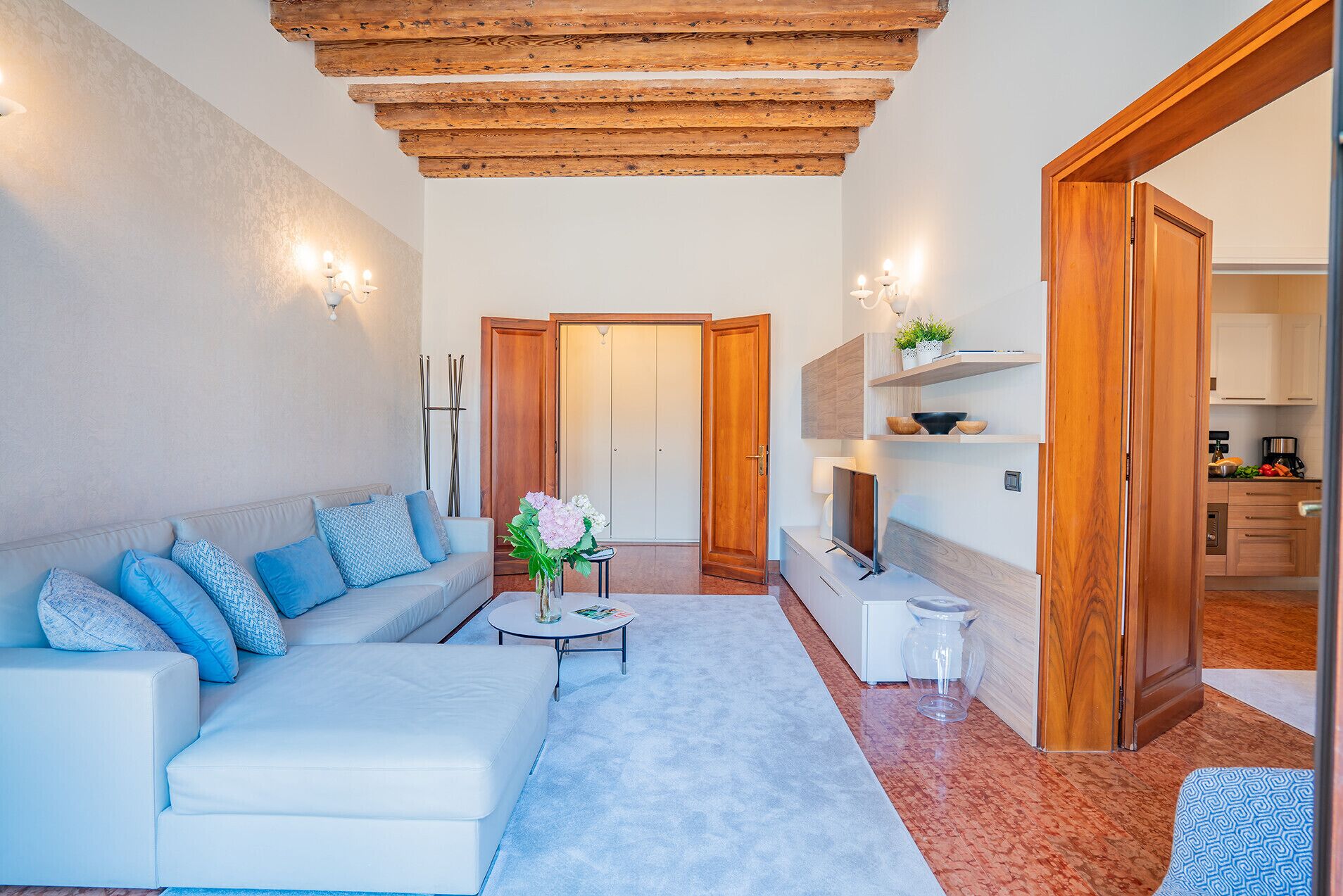 Un salon moderne avec un canapé, une table basse et un téléviseur. Le plafond est en bois et une porte donne accès à une autre pièce.