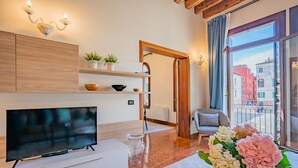 A modern living room with a TV, wooden cabinets, a glass coffee table, and a balcony with a view of buildings. - Ca' Del Monastero 1 Collection with Balcony (Venice)