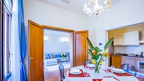 A dining area with a round table set for four, a kitchen in the background, and a living room with a sofa and coffee table. - Ca' Del Monastero 1 Collection with Balcony (Venice)