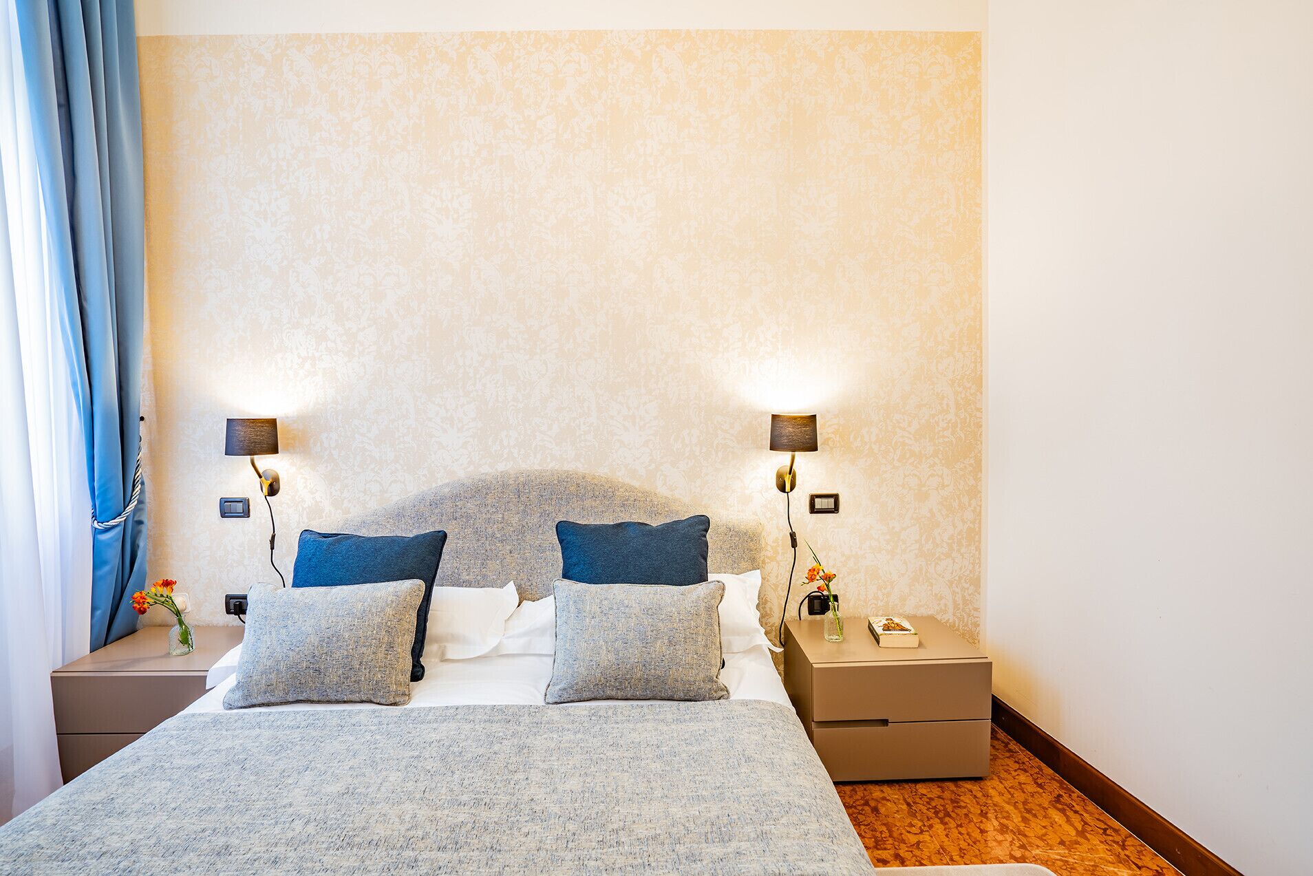Une chambre d’hôtel comprenant un lit, deux tables de chevet, une petite table et une lampe fixée au mur.