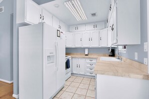 A kitchen with white cabinets, a built-in oven, a refrigerator, and a countertop with a coffee maker.