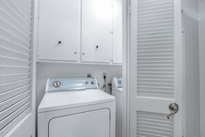 A laundry room with two white washers and dryers, a white door with a silver handle, and a white wall with a power outlet.