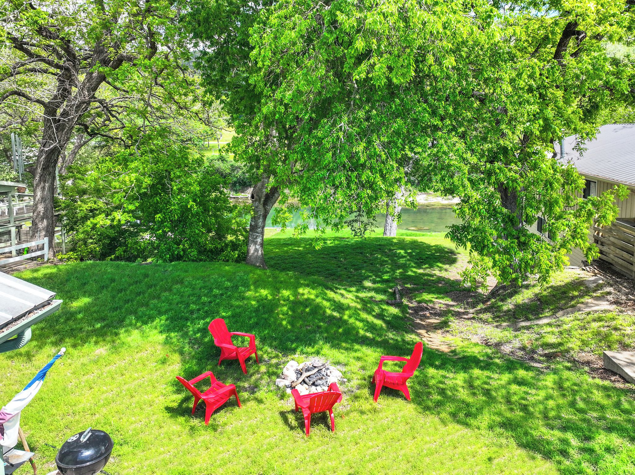 A backyard with a grill, red chairs, and a fire pit.
