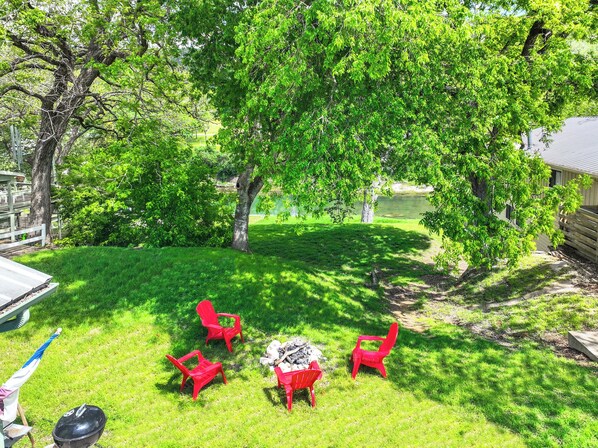 A backyard with a grill, red chairs, and a fire pit.