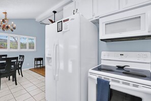 A kitchen with a white refrigerator, stove, and microwave. There is a dining table with chairs and a chandelier.