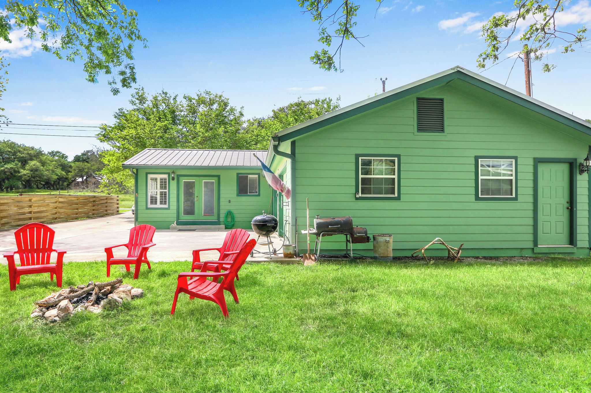 A green house with a porch, red chairs, a grill, and a flag.