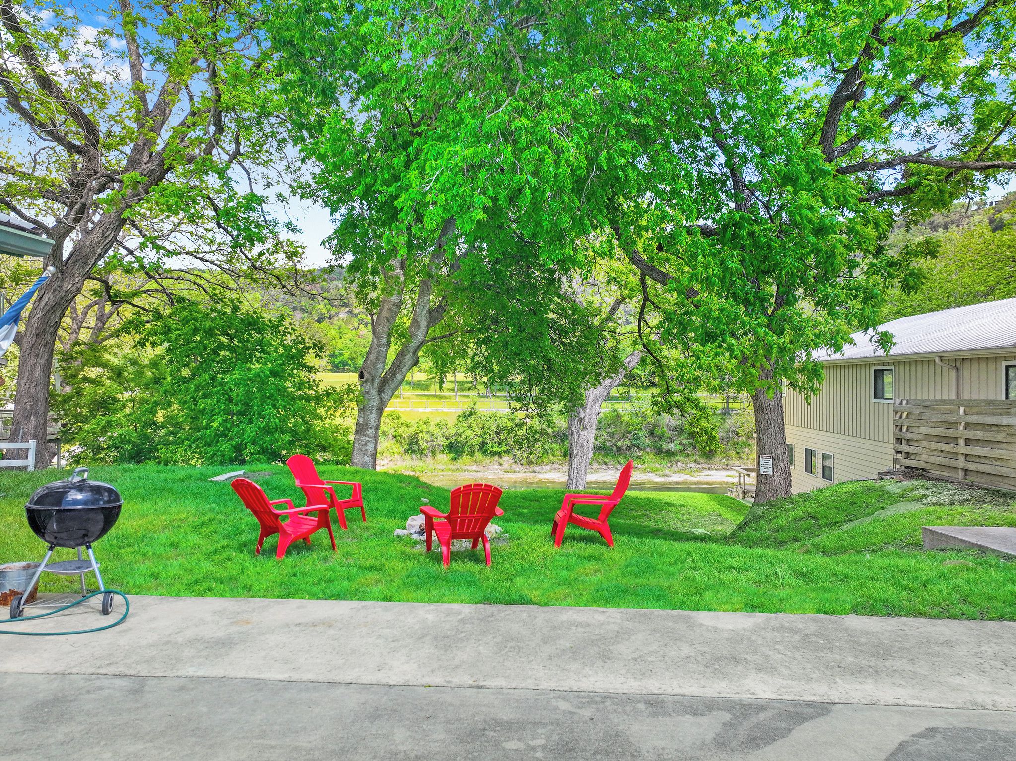 A backyard with a barbecue grill, red Adirondack chairs, and a wooden fence.