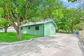A green single-story building with a sloped roof, a small porch, and a concrete driveway.