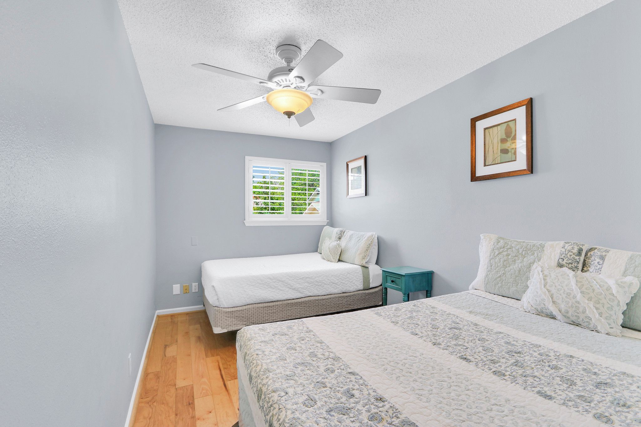 A bedroom with two beds, a ceiling fan, a window, and a small table.