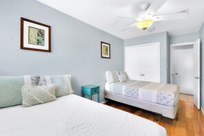 A bedroom with a bed, a nightstand, a ceiling fan, and two framed pictures on the wall.