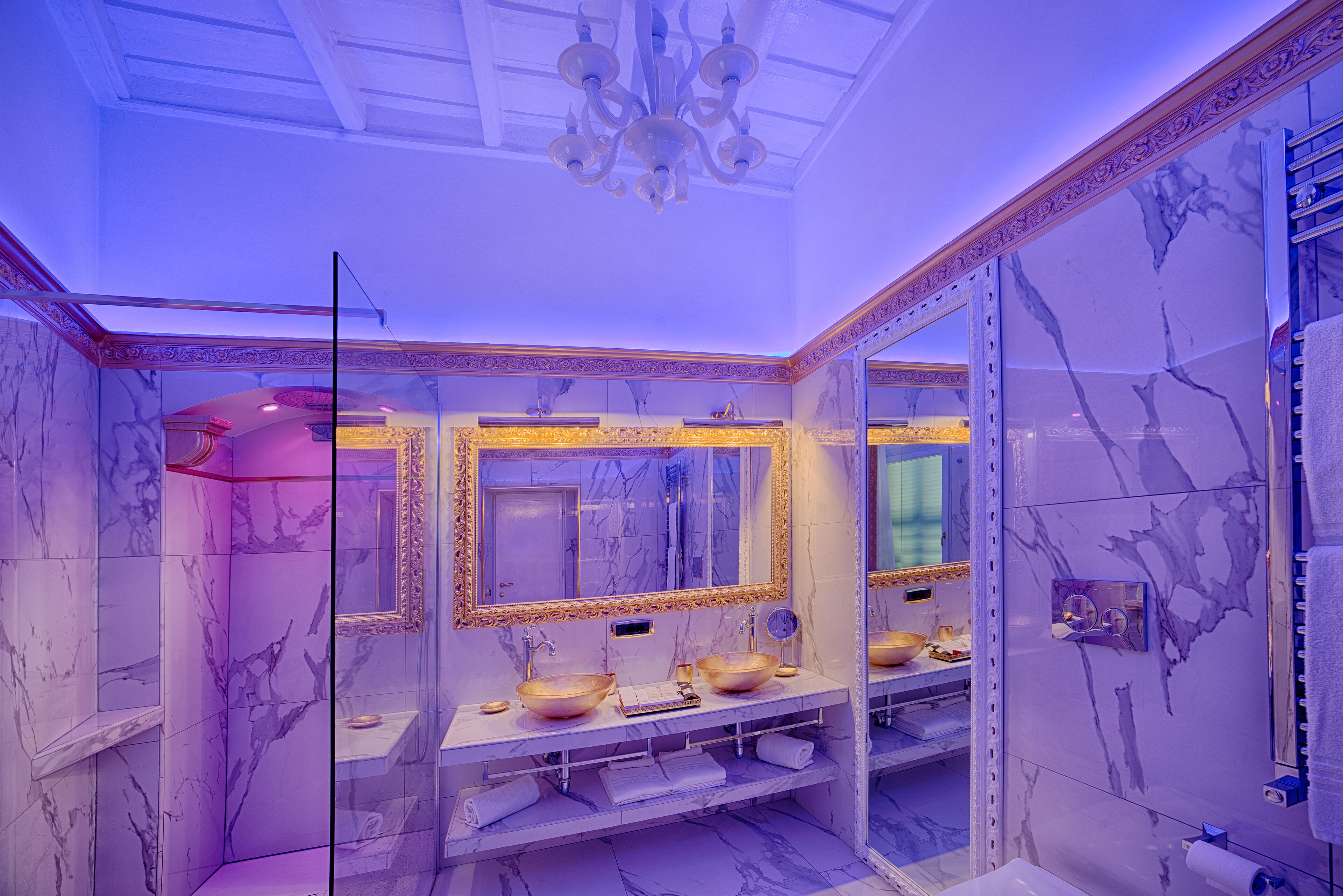 A luxurious bathroom with marble walls, a large mirror, and a chandelier.