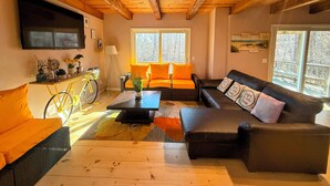 Una sala de estar acogedora con techo de madera, un ventanal grande, un sofá, una mesa de centro y un televisor montado en la pared.