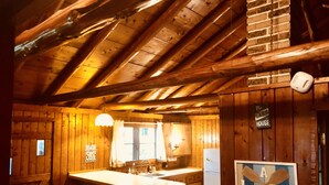 A wooden cabin interior with a kitchen area featuring a wooden bar, a refrigerator, and a sign reading "The Lake House".
