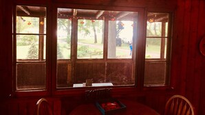 A room with a wooden interior, a table with a box of fruit, and a view of a grassy area through large windows.