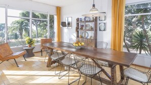 Un comedor con una mesa de madera, sillas de malla metálica, una planta en maceta y un cuenco de fruta.