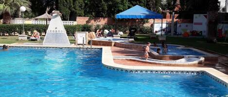 A swimming pool with a water slide, lounge chairs, and a blue canopy.