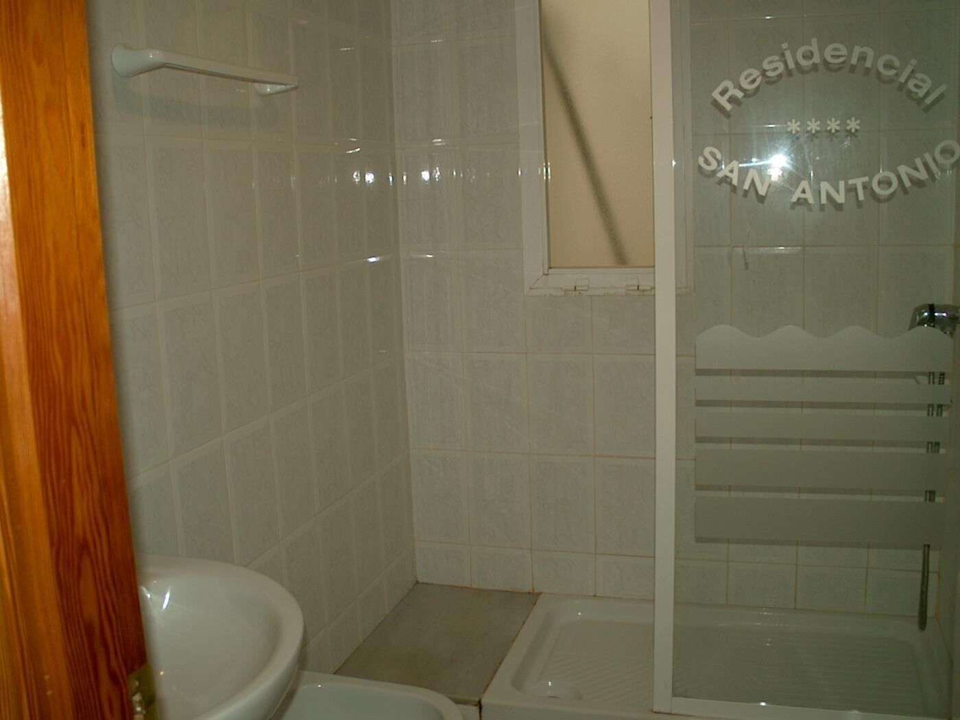 A bathroom with a toilet, a shower, and a glass door with text.