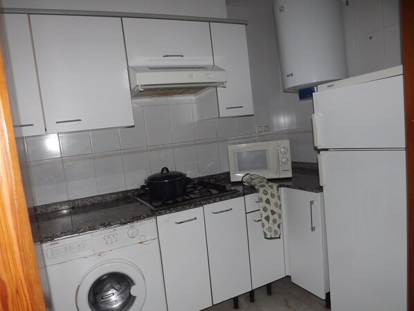 A compact kitchen with white cabinets, a microwave, a stove, and a washing machine.